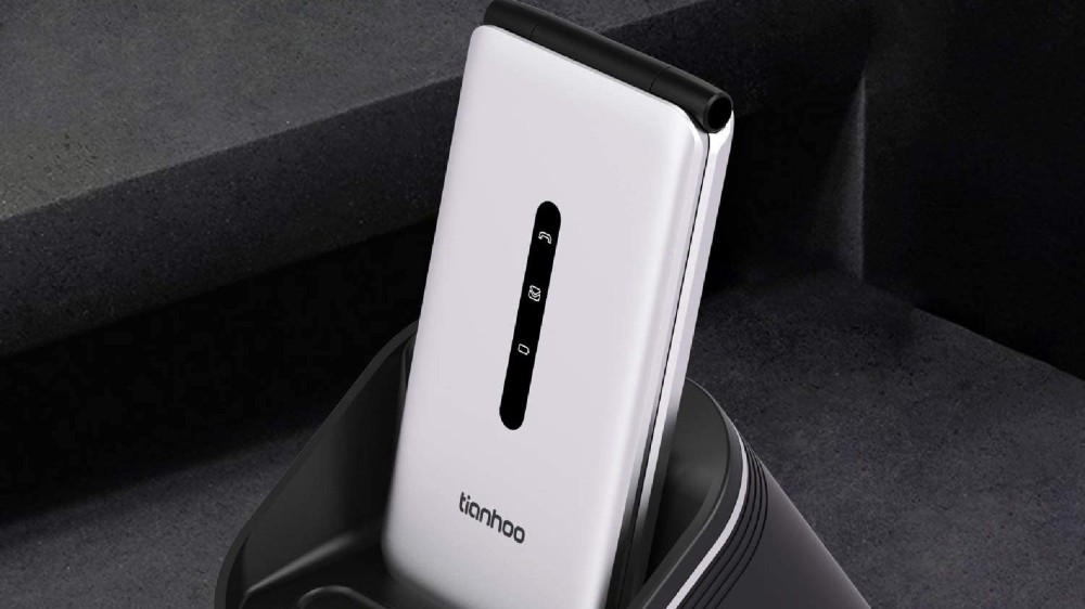 A white flip phone rests in its charging dock.