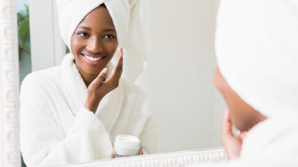 A woman applies cream to her face.