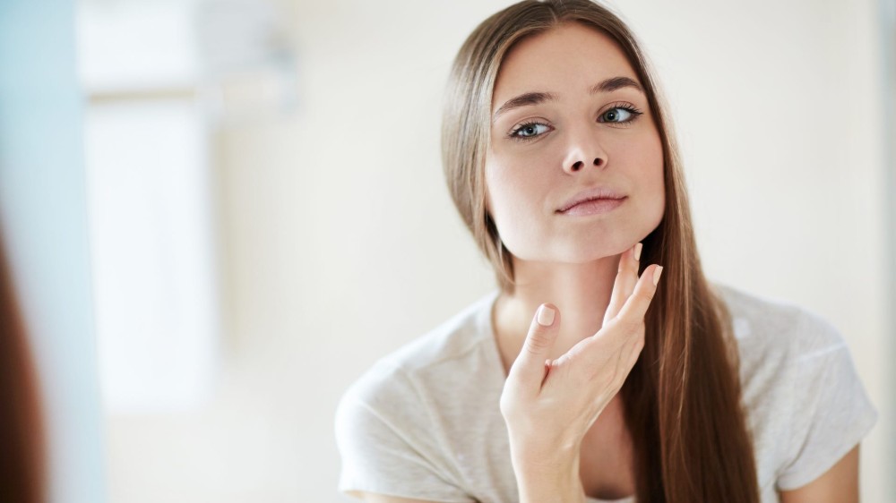 A woman examines her face in a mirror.