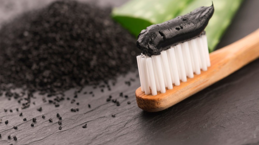 A toothbrush with black charcoal toothpaste on it and charcoal particles in the background.