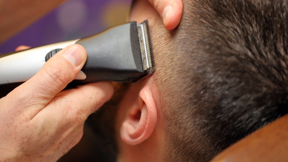 A person uses a hair trimmer on a man's hair.