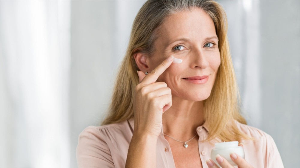 A woman applies a face cream under her eye.