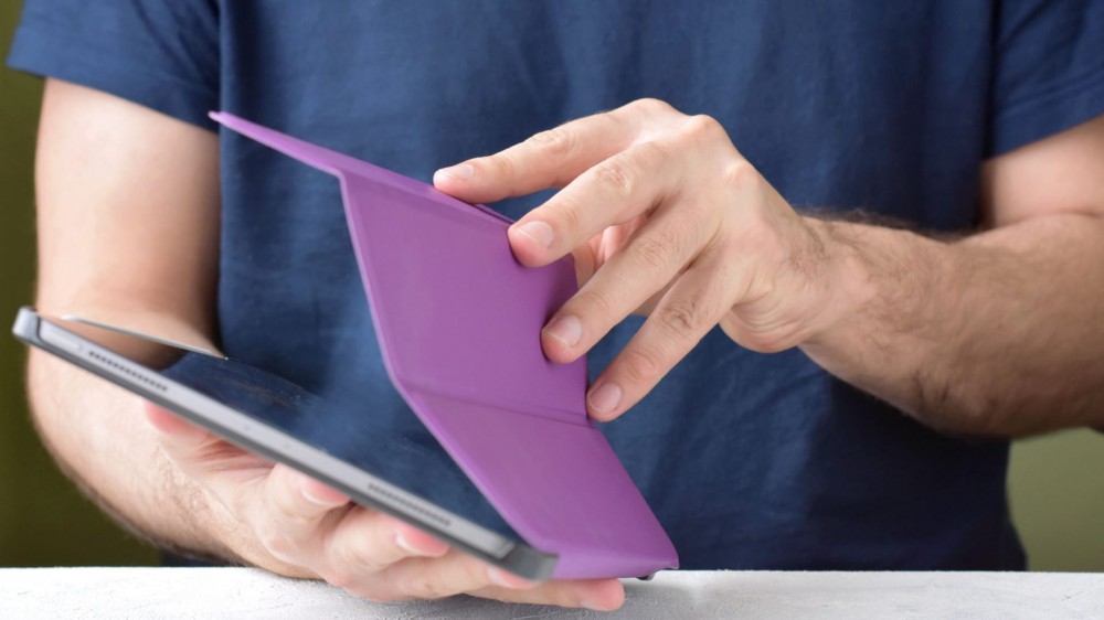 A man opens up an iPad with a purple case on it.