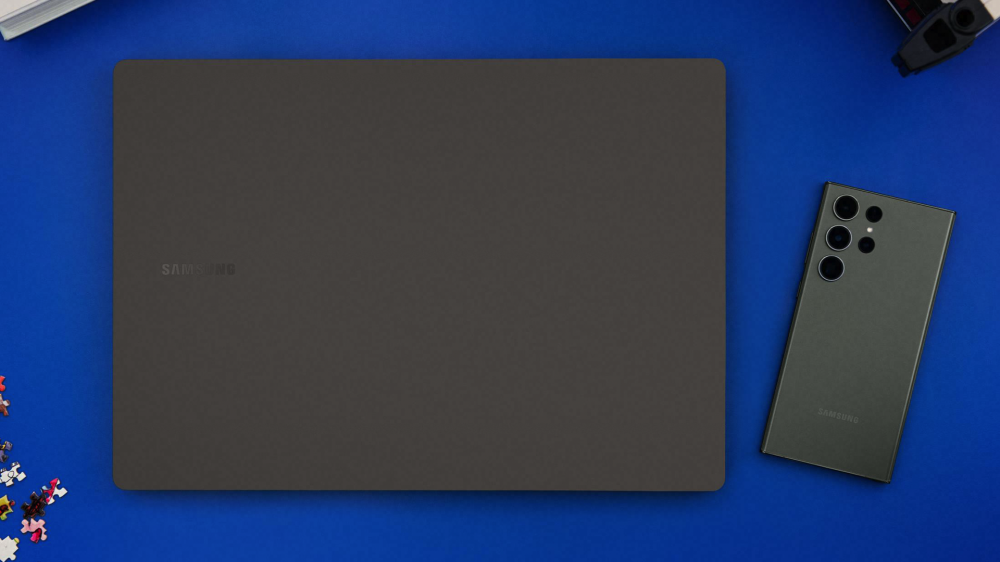 The Samsung Galaxy Book 3 Ultra closed on a blue table with an S23 Ultra smartphone.