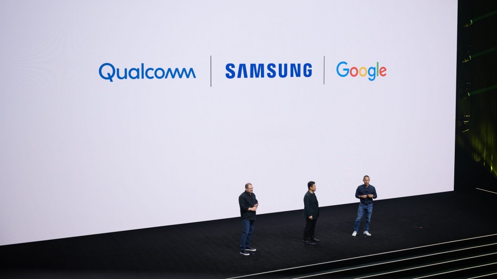 TM Roh, Cristiano Amon, and Hiroshi Lockheimer presenting at Galaxy Unpacked 2023 with Qualcomm, Samsung, and Google logos on the screen