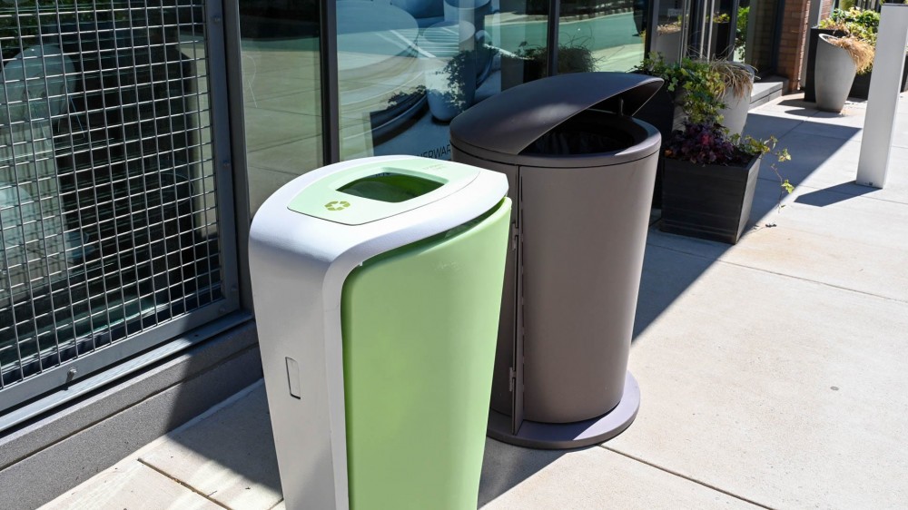 A trash can and recycling can on the sidewalk of a downtown